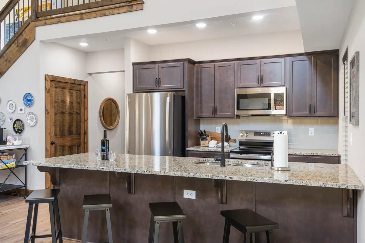 This image displays a stylish, modern kitchen with a granite countertop, dark cabinetry, stainless steel appliances, and a central island. The open design invites participation in cooking and socializing.