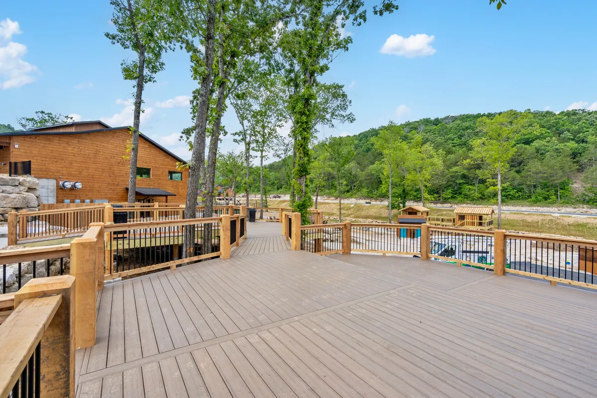 A spacious wooden deck is surrounded by trees, with distant hills visible in the background. The area is serene and private, making it an ideal spot to relax after a day of exploring, perhaps with a pet napping nearby.