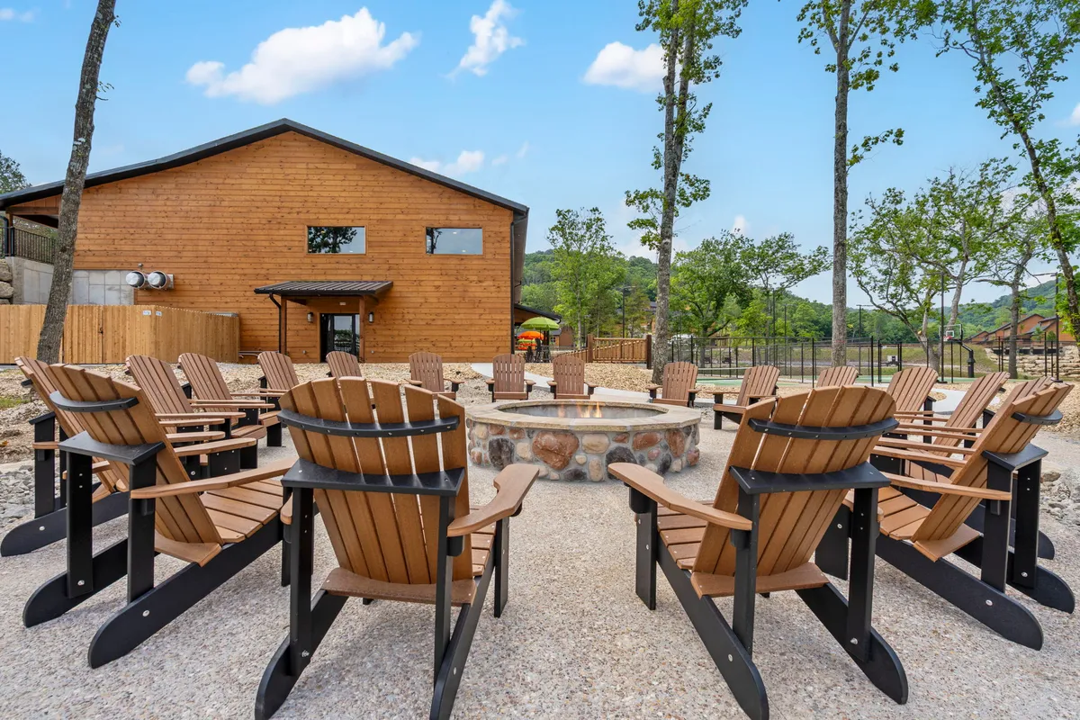 A welcoming exterior scene featuring a wooden cabin with a cozy fire pit surrounded by Adirondack chairs. The peaceful setting encourages groups to gather outdoors for conversation, storytelling, or stargazing, with the cabin’s inviting structure in the background.