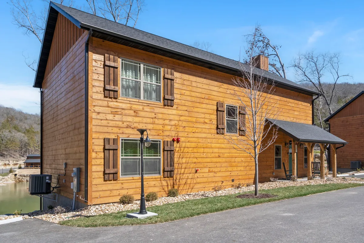 The exterior of the cabin featuring expansive windows, a welcoming front porch, and landscaped yard set against a serene natural backdrop. The inviting facade encourages guests to imagine mornings with coffee outside or evenings spent reconnecting with friends and family.