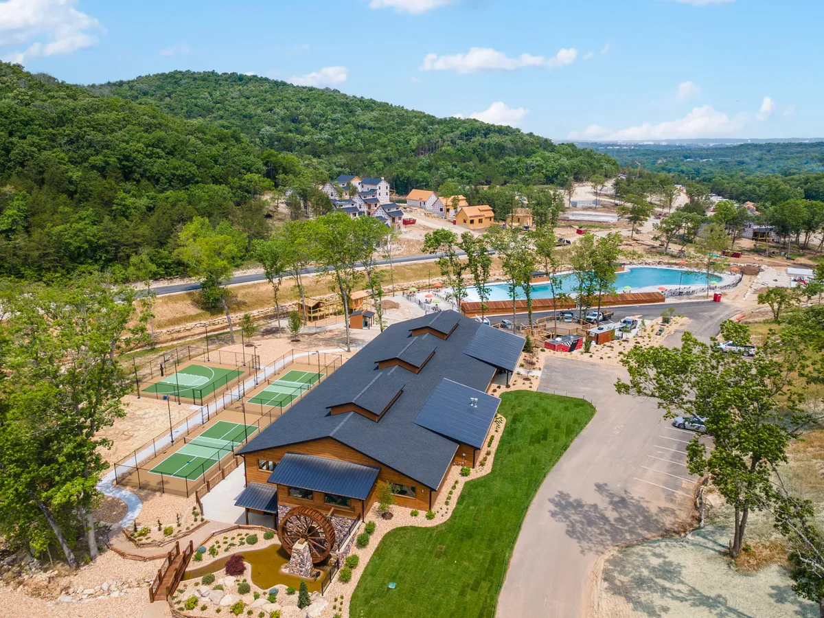 The main building sits alongside a swimming pool, tennis courts, and beautifully landscaped gardens, with a water wheel feature creating a resort-like, communal atmosphere ideal for outdoor recreation and relaxation.