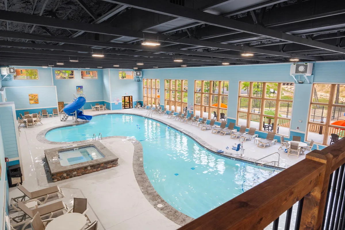 A bright, family-friendly indoor pool with a large water slide, hot tub, and lounge chairs. The space is lively, filled with natural light from large windows, and invites families to spend time swimming, playing, and relaxing together, regardless of the season.