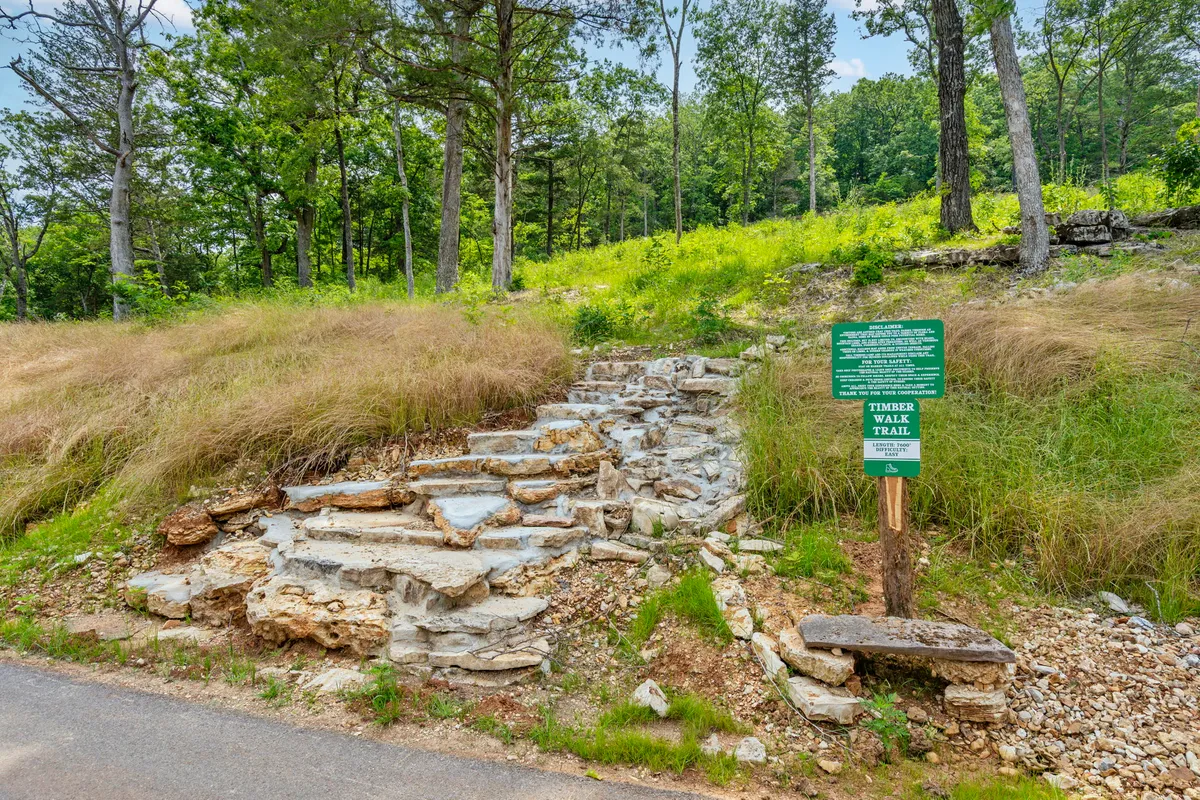 Stone steps lead up to a trail sign amidst dense greenery, inviting guests into the surrounding forest for hiking and nature walks. The path looks well-kept and accessible, highlighting easy opportunities for outdoor exploration.
