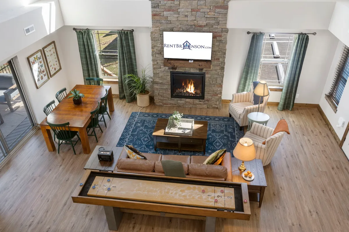 This image highlights a warm living and dining area featuring a fireplace, a roomy dining table, a comfortable sofa, and a television. The space is arranged to foster family gatherings, game nights, and relaxation.